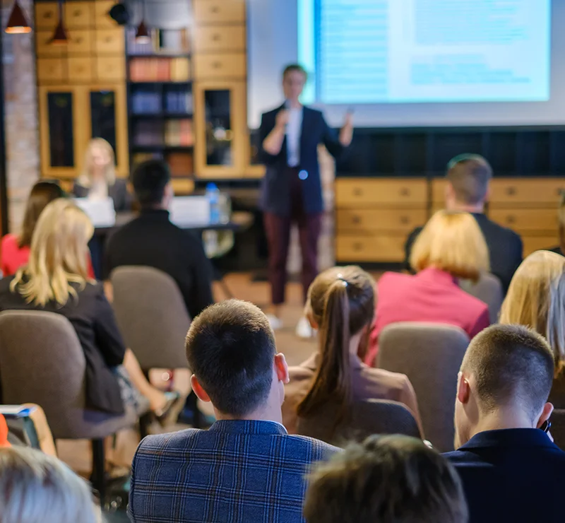 Group of people sitting listening to speaker at an event.