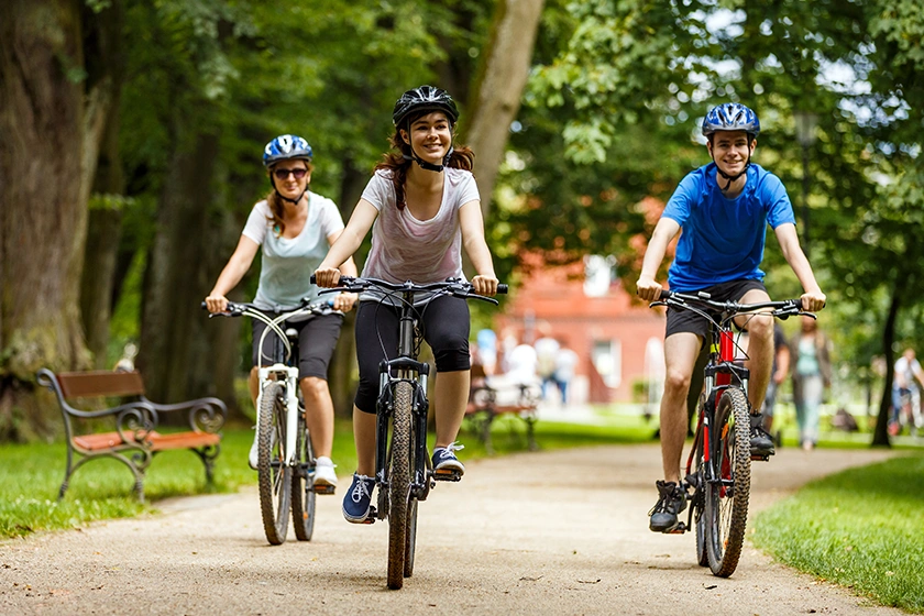 Family cycling through green park with trees.