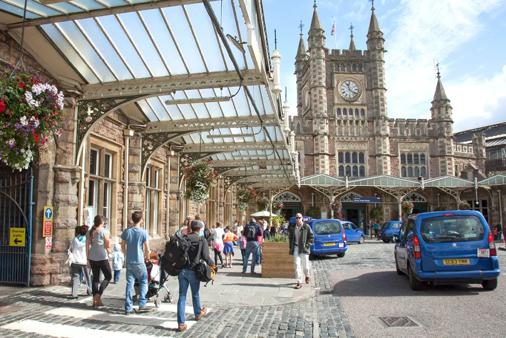 - Station Approach at Bristol Temple Meads station. Passengers walk towards the station. On the right, a queue of blue taxis waits.